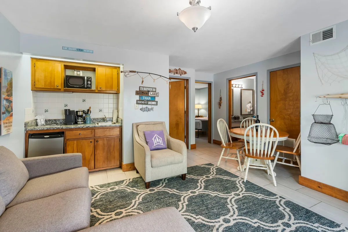 A view of the kitchenette area opens up to a dining table and a sofa, with decorative elements on the walls. The setting is cozy, suggesting an inviting space for both meal preparation and shared dining.