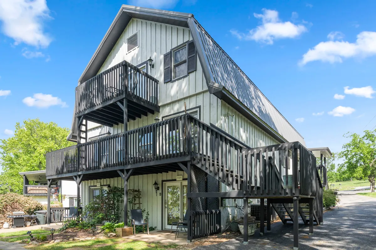This image features two large balconies overlooking lush landscaping, with exterior wooden stairs connecting the spaces. The scene hints at spacious outdoor areas designed for gatherings, relaxation, and enjoying the outdoors with friends and family.