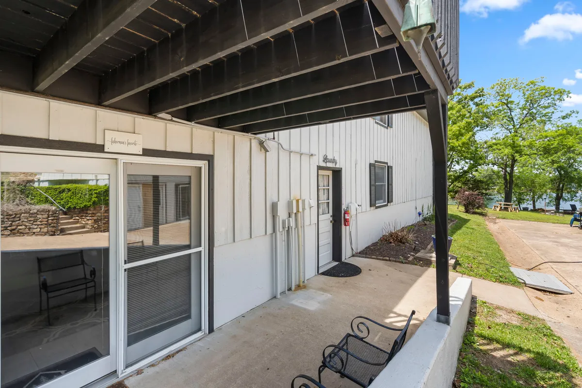 The inviting entrance of a lakeside property, framed by windows and a landscaped seating area, hints at the welcoming vibe inside. The view showcases a tranquil space for gathering, relaxing, or enjoying views of the water, connecting the inside experience to the outdoors.