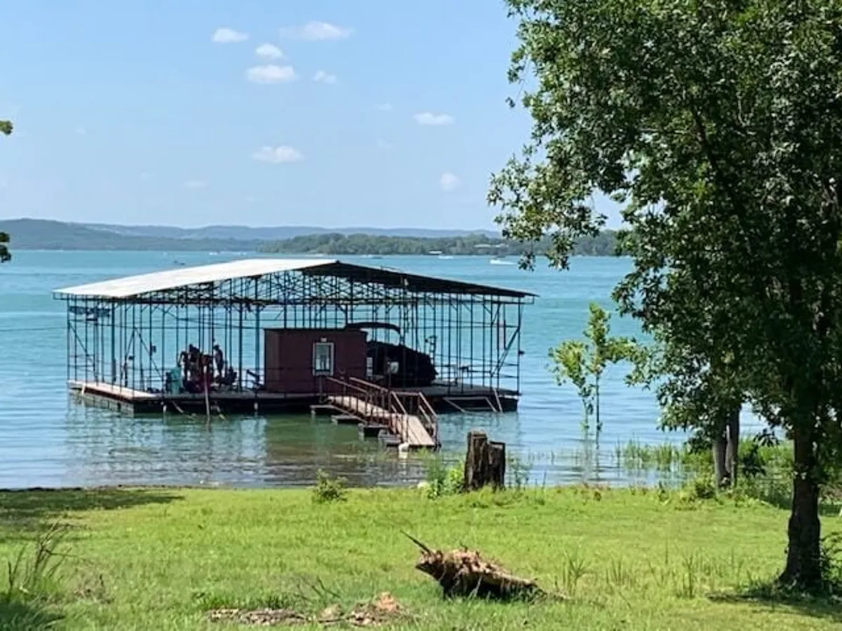 A wooden dock stretches over the water, with a boathouse and trees framing the scene. The dock provides ample space for fishing, swimming, and family picnics, set against a relaxed lakeside background. The environment feels inviting for both peaceful mornings and lively group activities.